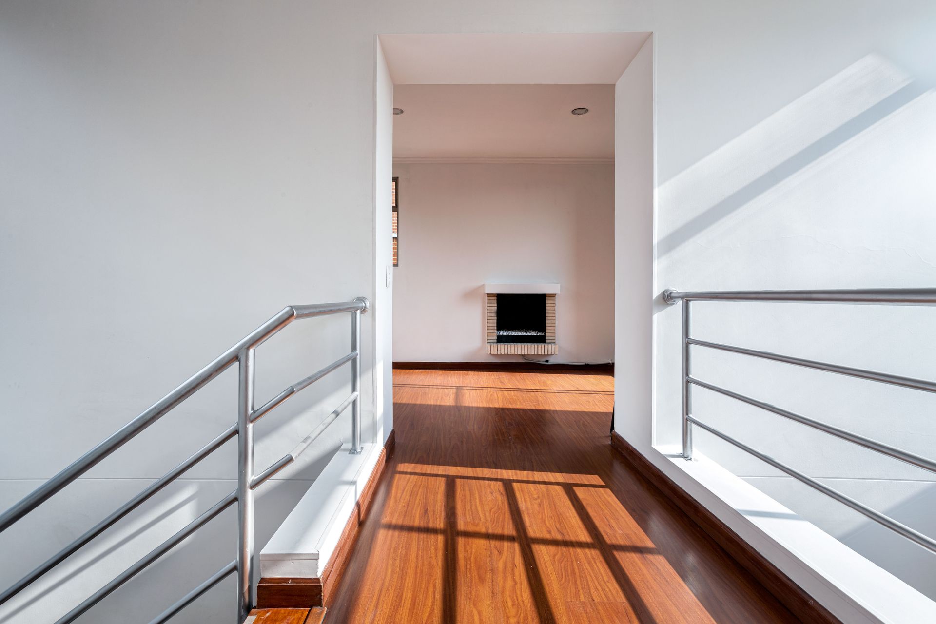 Bright and minimalistic hallway with railings and wooden floor in Bogotá apartment.